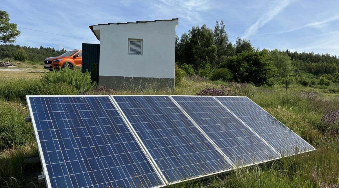 Solar panels in countryside with car and small building in the background.