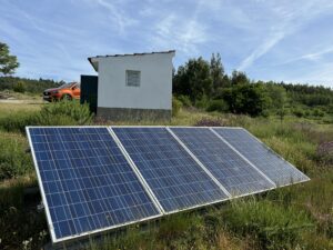 Solar panels in countryside with car and small building in the background.